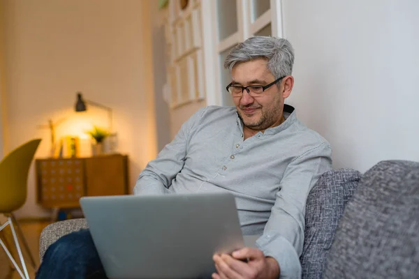 Człowiek Siedzi Kanapie Przeglądając Netto Laptopie Domu — Zdjęcie stockowe