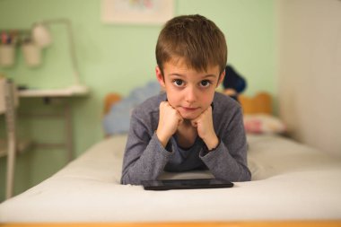 çocuk odada yatakta yatıyordu ve tablet kullanarak