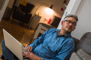 Orta yaşlı gri saçlı adam kullanarak laptop içinde rahat daire