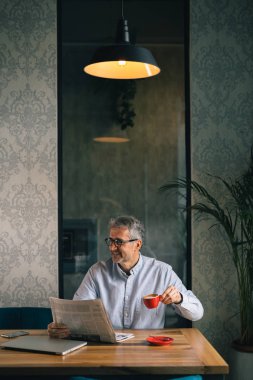 Gülümseyen işadamı gazete okuyor ve modern kafe barda kahve içiyor.