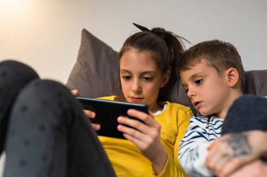 Erkek ve kız kardeşi yatakta döşeme ve tablet kullanarak