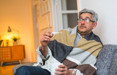 Şok hasta adam oturma kanepe ve termometre bakıyor