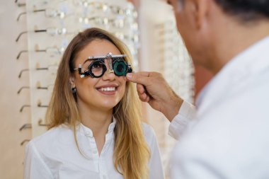 Kadın deneme çerçevesi giyiyor ve gözlükçü bakıyor. 