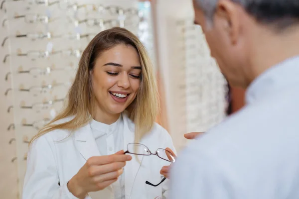 Mulher óptica ajudando cliente a escolher melhor óculos para ele — Fotografia de Stock