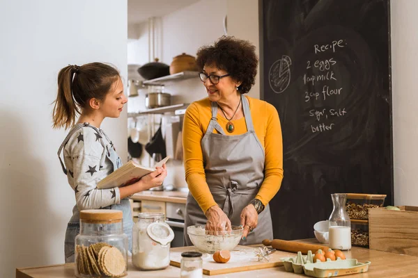 granddaughter and grandmother cooking together in home kitchen