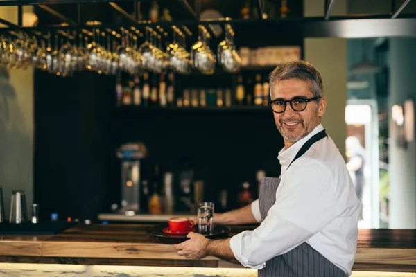 Waiter holding plate with coffee and water in cafe bar