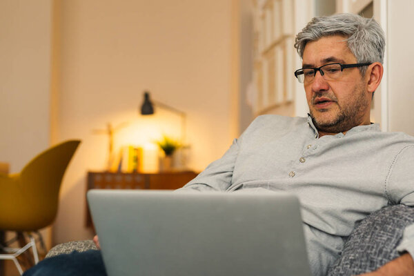 Man sitting on sofa and browsing net on laptop in home