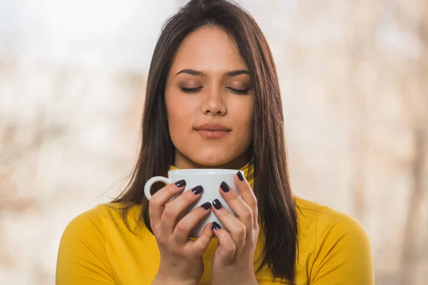 Portrait of woman in yellow jumper with closed eyes smelling coffee