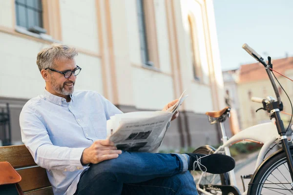 Mature man reading newspaper outdoor in city