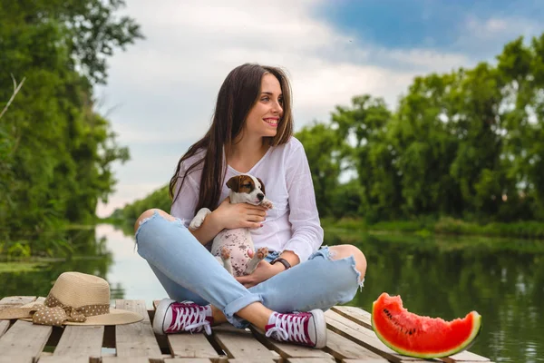 Kvinna njuter sommardagar med sin valp, sitter på floden docka — Stockfoto