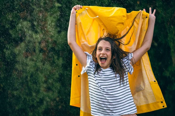 Girl with yellow raincoat in hands shouting enjoying rainy daytime