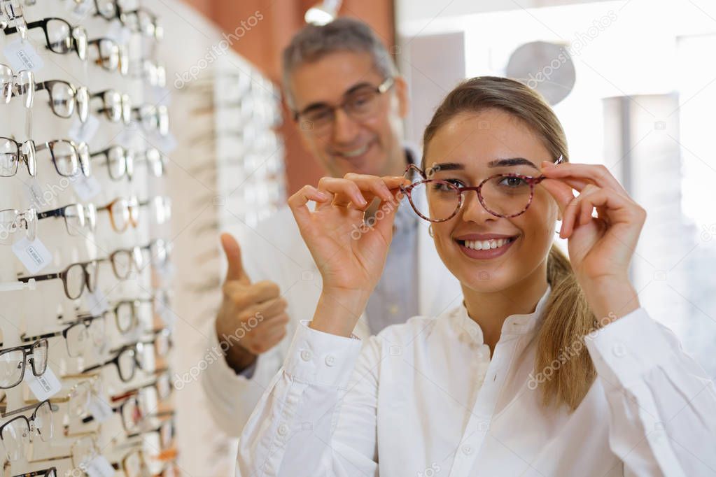 Woman and optician in store, lady trying on eyeglasses.