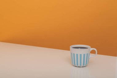 Bej ve turuncu arka plan üzerinde mavi çizgili beyaz kupa kahve