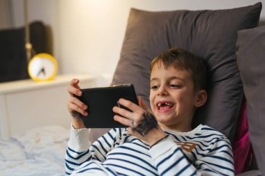 Küçük çocuk evde yatıp tablet kullanıyor.