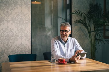 Kafeteryada tablet ve içme kahvesi kullanan gri saçlı işadamı