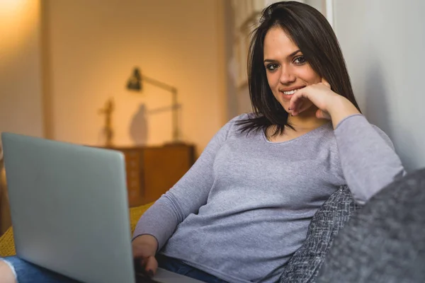 Woman enjoying lazy afternoon at home, relaxed on sofa and using laptop.