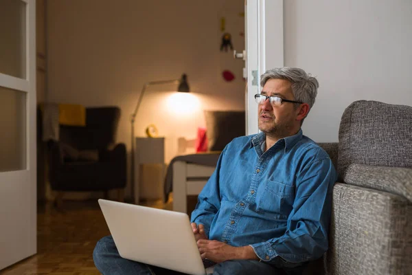 Чоловік сидить на підлозі і використовує ноутбук у себе вдома — стокове фото
