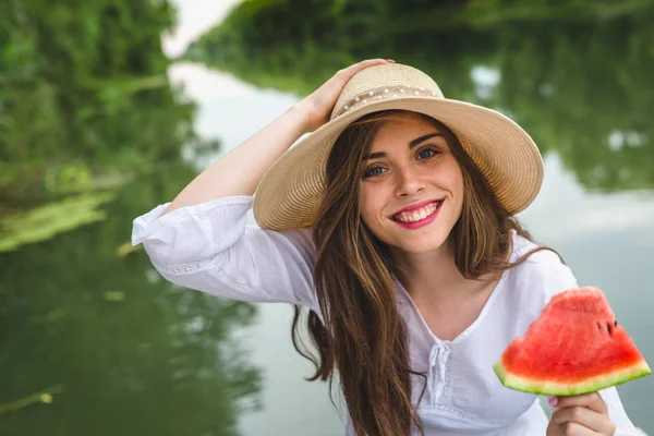 Vacker kvinna äter vattenmelon utomhus vid floden — Stockfoto