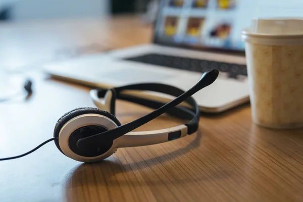 Headphones with microphone and laptop on desk, customer support concept.