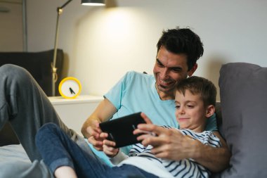 baba ve oğlu evde tablet üzerinde oyun oynuyor