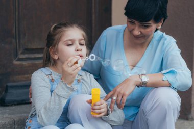 Anne ile şehirde sabun balonu şişiren çocuk.