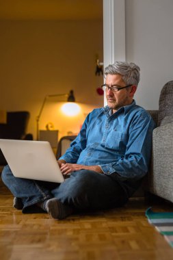 Casual Weekend, adam evde oturma yerde dizüstü bilgisayar kullanarak.