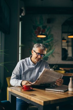 Başarılı gri saçlı adam kafeteryada kahve molası gazete okuma