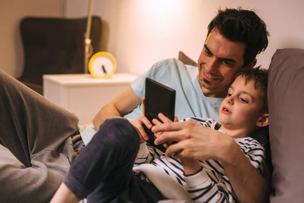 Father and son laying on bed and using tablet at home — Stock Photo, Image