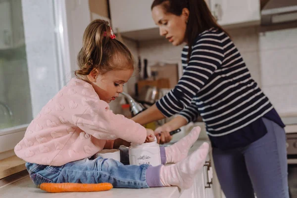 little girl making mess in kitchen while mother preparing lunch