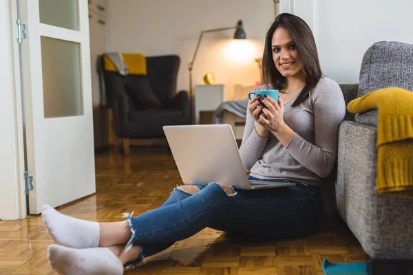 Relaxed woman using laptop and drinking coffee at home