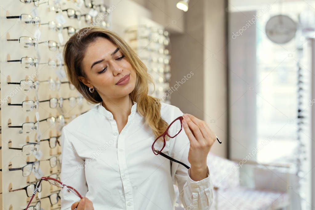 Pretty young woman choosing glasses in optic store.