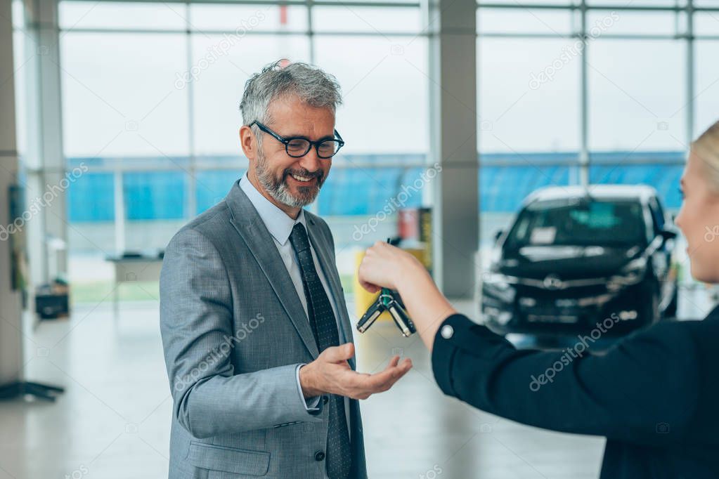 Saleswoman giving car keys to a client at car showroom