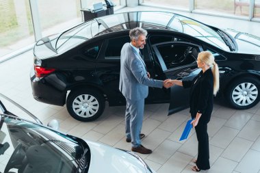 Araba galerisinde müşteriyle el sıkışan bir temsilci.