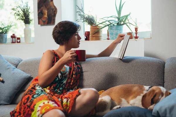 Frau Entspannt Auf Sofa Mit Hund Buch Lesen Und Kaffee — Stockfoto