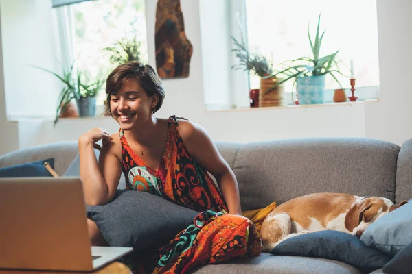 Woman relaxing on sofa with dog using laptop