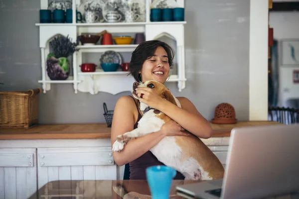 woman holding dog in lap and using laptop at home