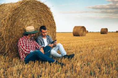 Olgun çiftçi ve genç meslektaşı buğday tarlasında tablet kullanıyor.