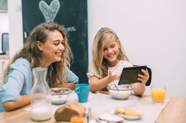Birlikte harika vakit geçiriyoruz. Anne ve kızı evde kahvaltı yaparken tablet kullanıyorlar.. 