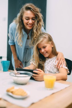 Anne ve kızı evde kahvaltı yaparken tablet kullanıyorlar.
