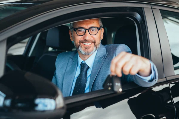 Son sınıf öğrencisi iyi giyimli arabada oturuyor ve araba galerisinde anahtarlarını tutuyor.