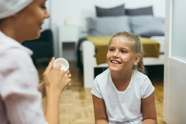 Mother applying face cream to daughter face at home