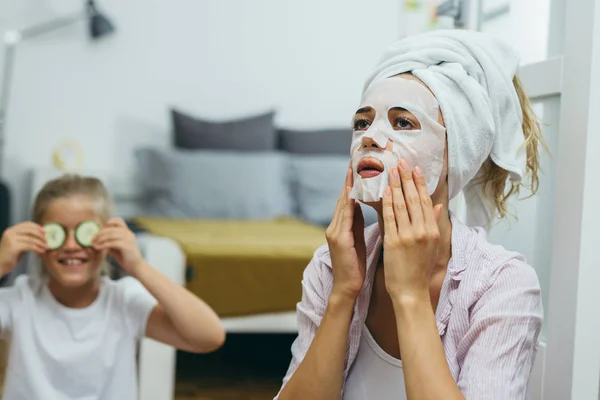 Kadınlar ve kızları evde kozmetik cilt bakımı yaparken eğleniyorlar. Kumaş yüz maskesi ve salatalıklı maske..