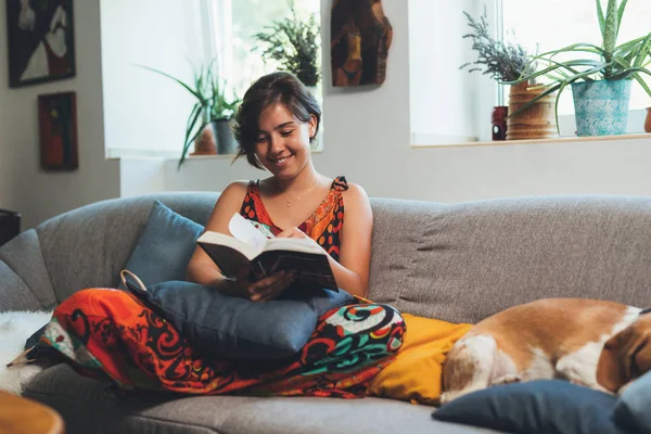 Kvinna avslappnad i soffa läsa bok hemma — Stockfoto