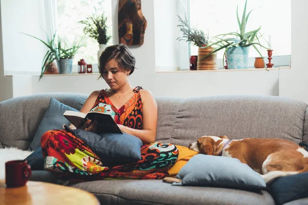Nő ellazult kanapén olvasás könyv otthonában — Stock Fotó