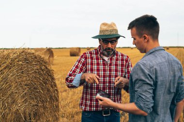 İki tarım işçisi ekili buğday tarlasında dışarıda konuşuyorlar.