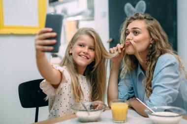 Family having breakfast, mother and daughter taking selfie at home.