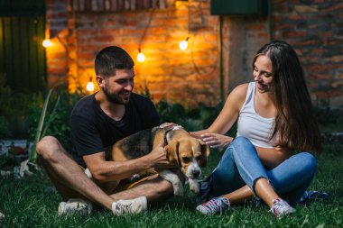 Evin arka bahçesinde köpekle oynayan genç çift.