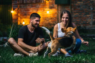 Evin arka bahçesinde köpekle oynayan genç çift.