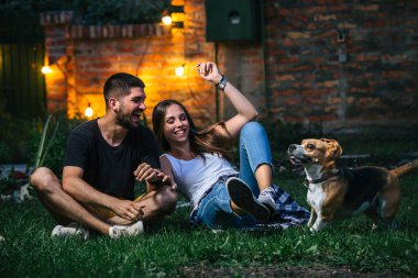 Evin arka bahçesinde köpekle oynayan genç çift.