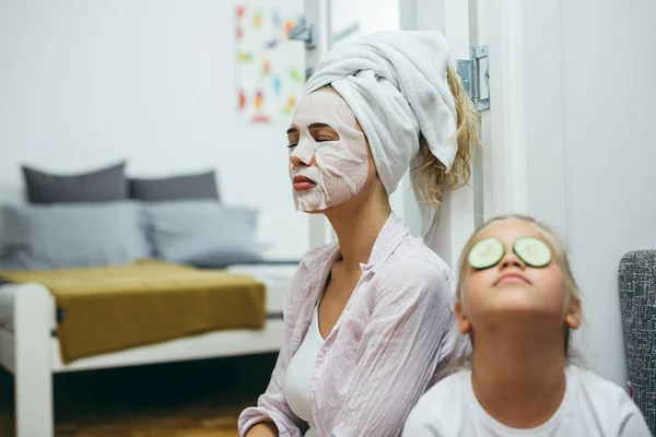 Anne ve kızı evde dinleniyor, yüz maskeleri takıyorlar..